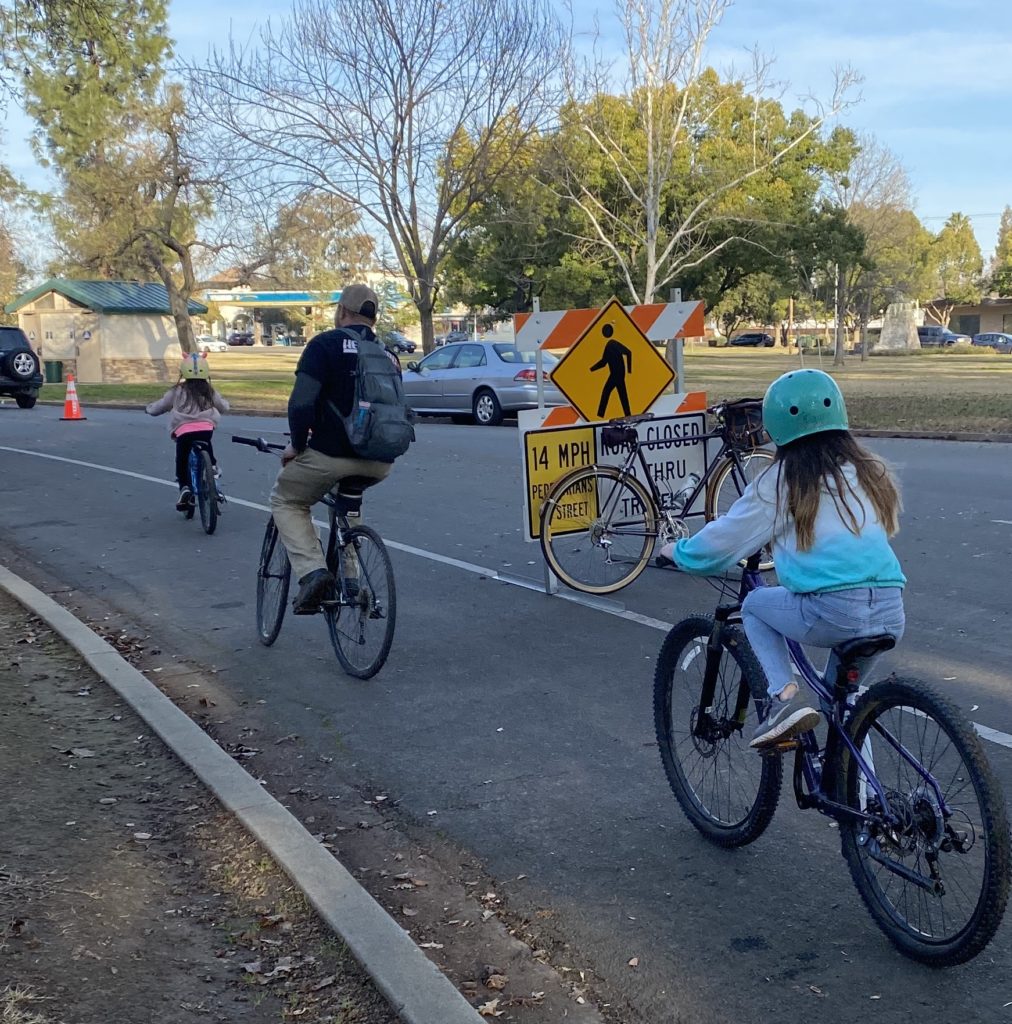 Two children and an adult ride their bikes down a street.