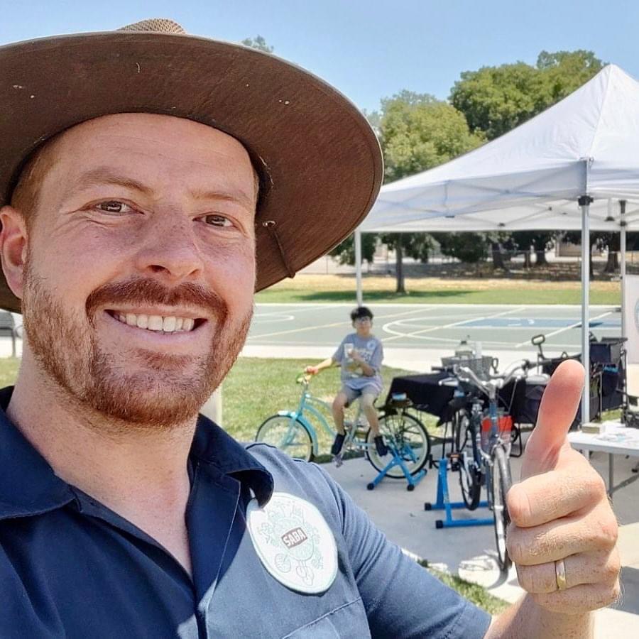 A man with a red beard and a sun hat gives a thumbs up.