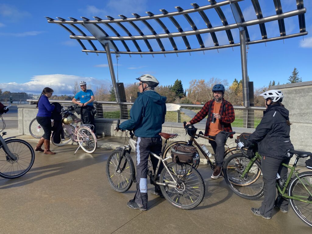 Five cyclists stand by their bikes next to the river.