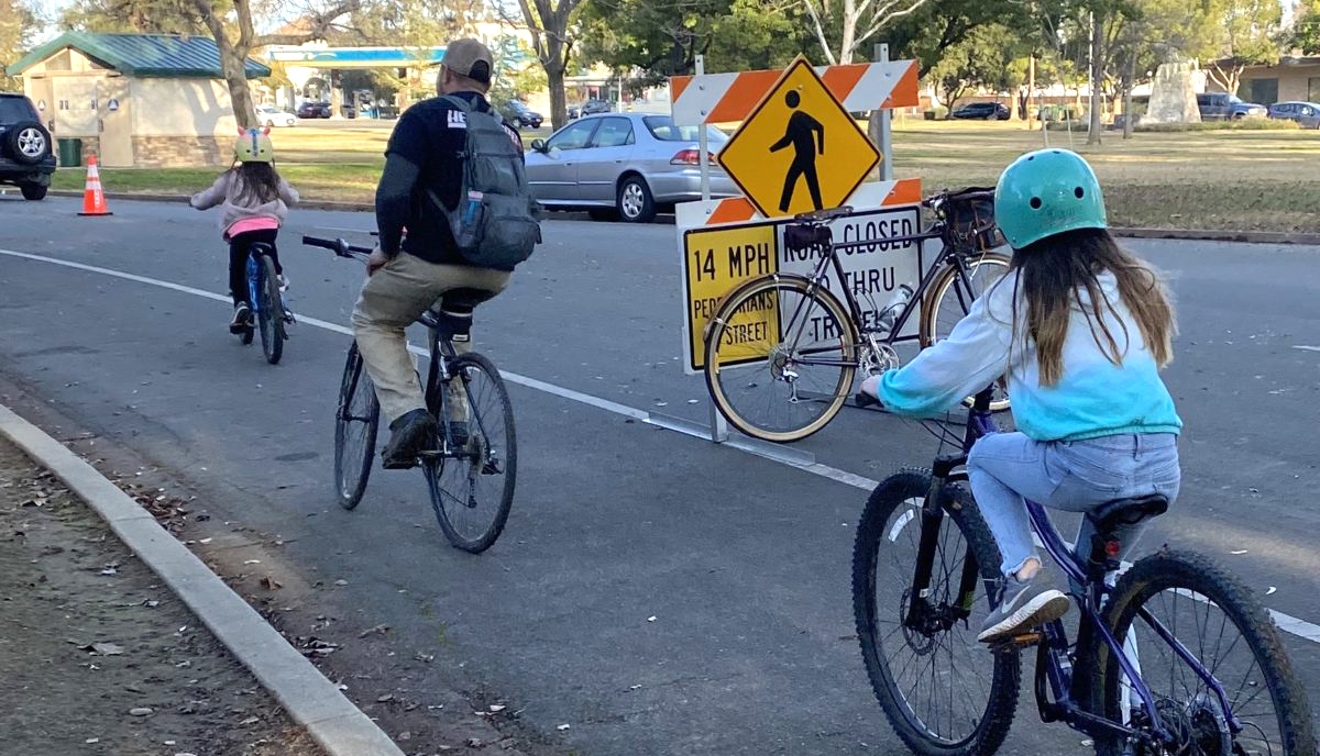 Two children and a man ride their bikes down a street.