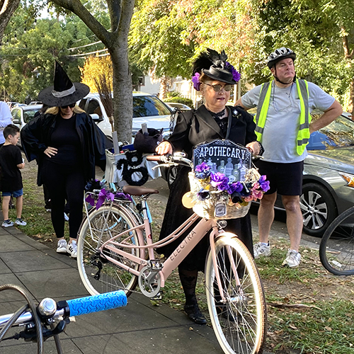 A woman dressed as an old time pharmacist stands next to her bicycle.