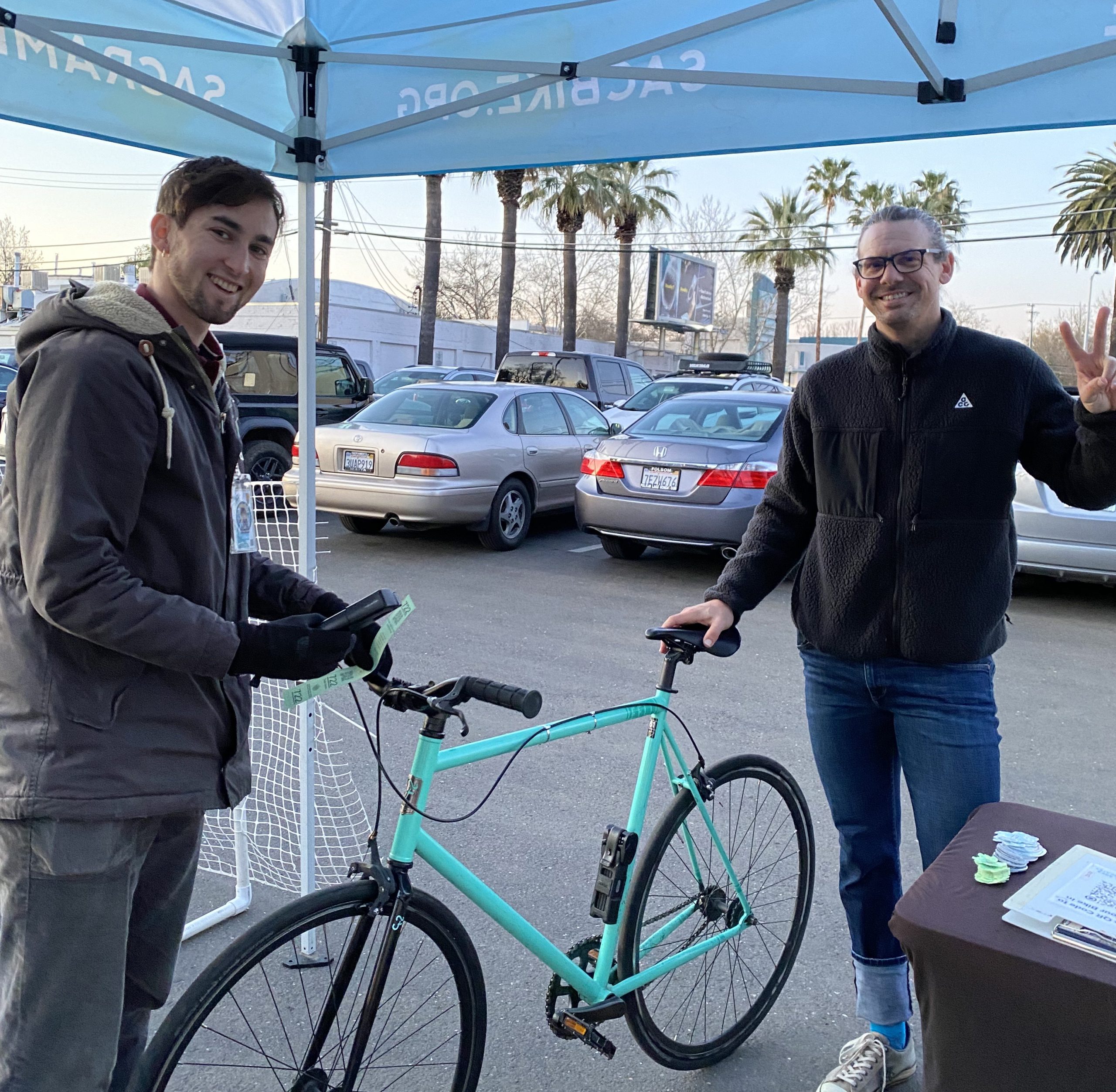Two men stand holding a bike under a canopy.