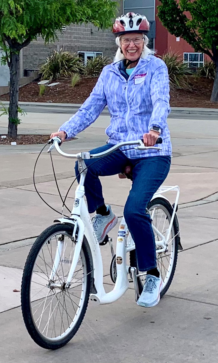 A woman wearing a bike helmet smiles as she sits on a bike.