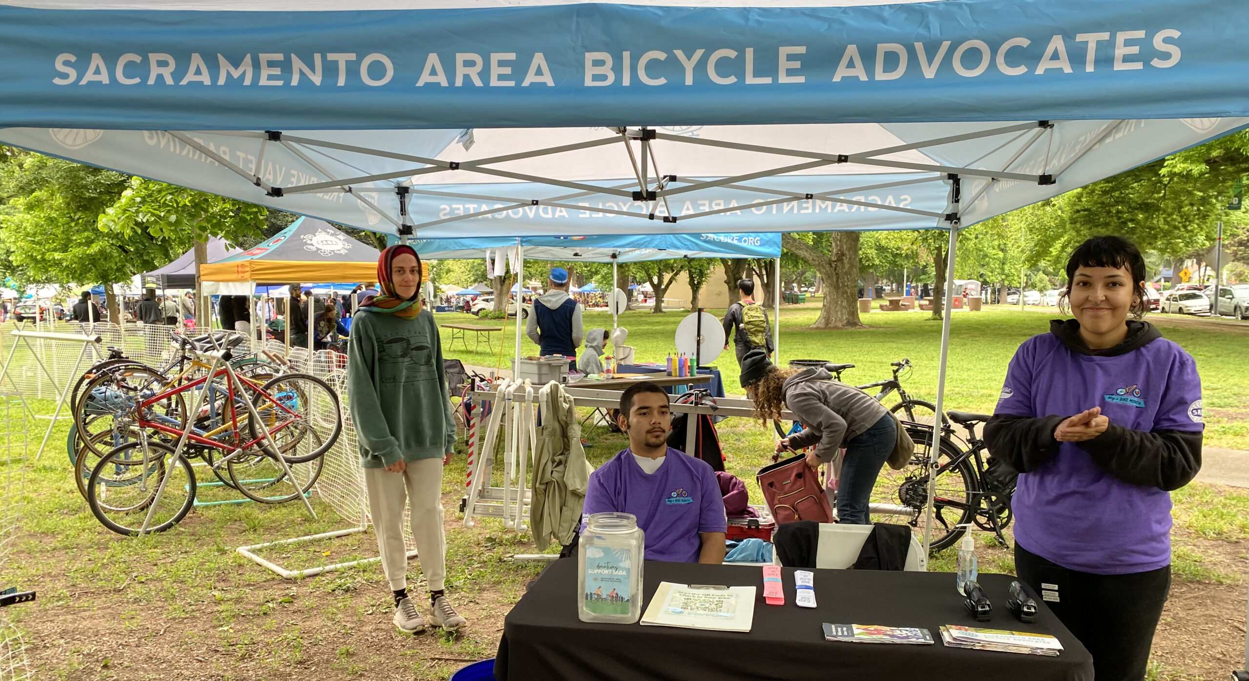 Three people stand under a tent with bikes parked behind them.