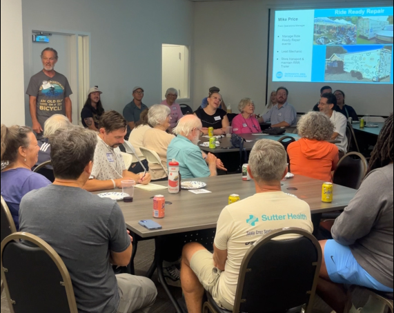 People sit in a room around tables looking at a presentation.