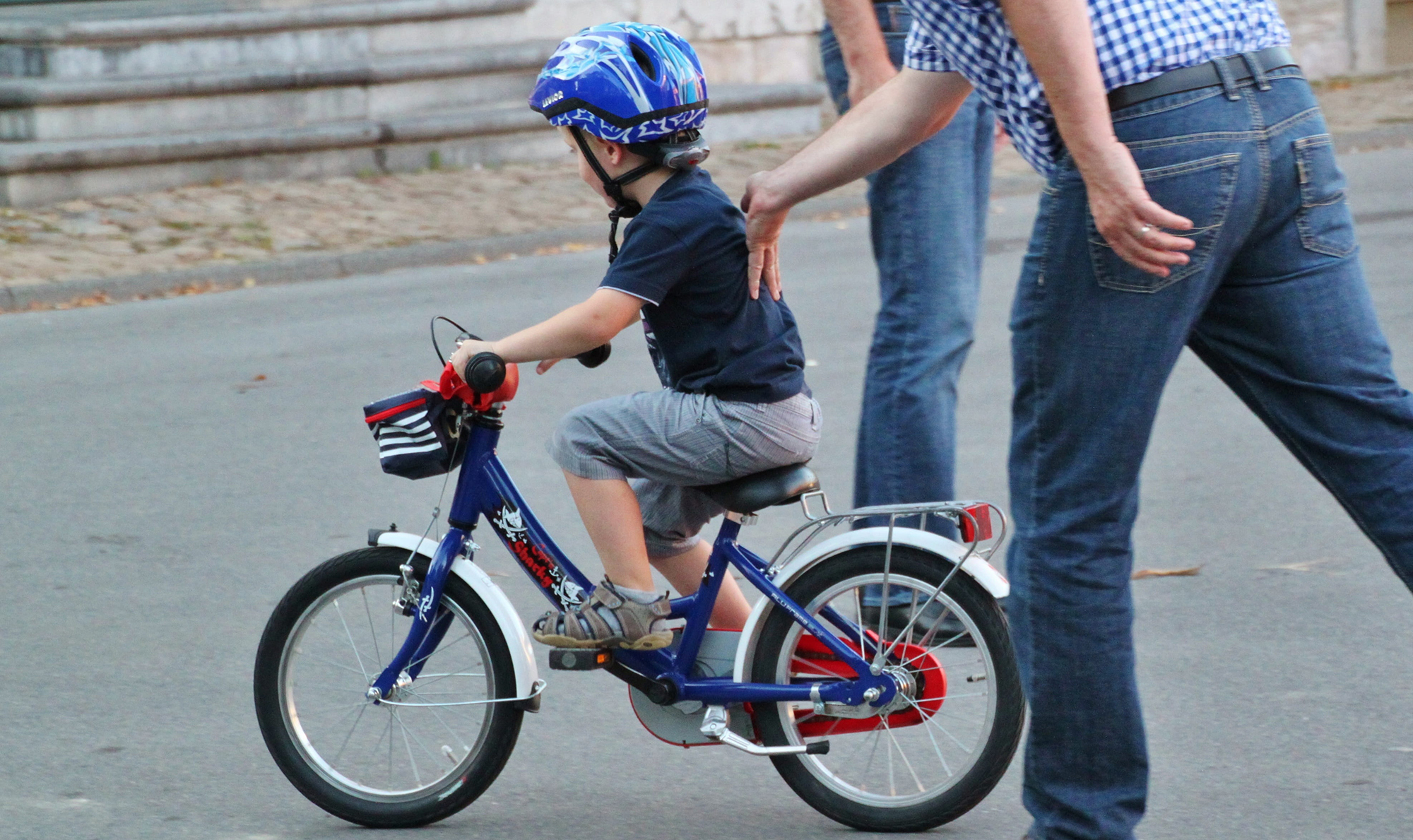 A small child on a bike is supported by an adult.