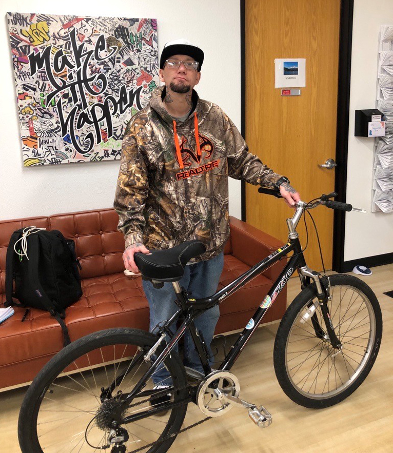 A man wearing a cap and jacket stands holding a new bicycle.