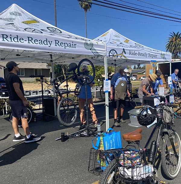 People repair bikes under a tent that says: Ride Ready Repair.