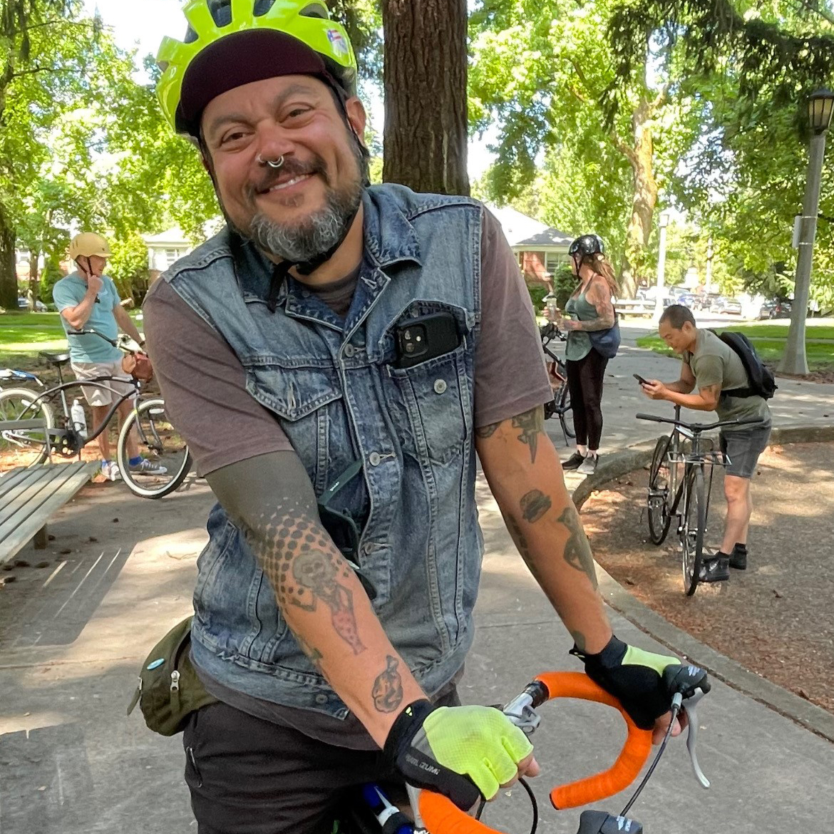 A man wearing a yellow helmet and a blue vest sits astride his bike.