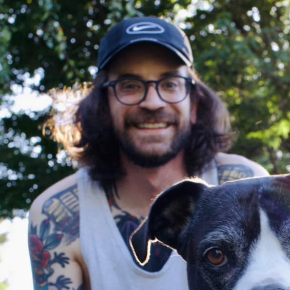 A man with glasses, long hair and a cap with a dog.